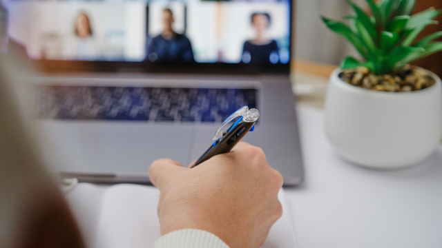 Hand mit Stift vor Laptop mit Videokonferenz