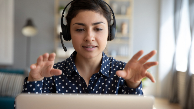 Frau mit Headset gestikuliert vor Monitor