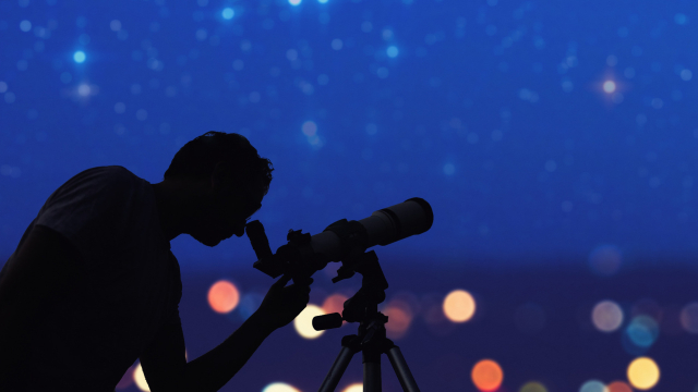 Silhoutte eines Mannes am Teleskop vor Sternenhimmel