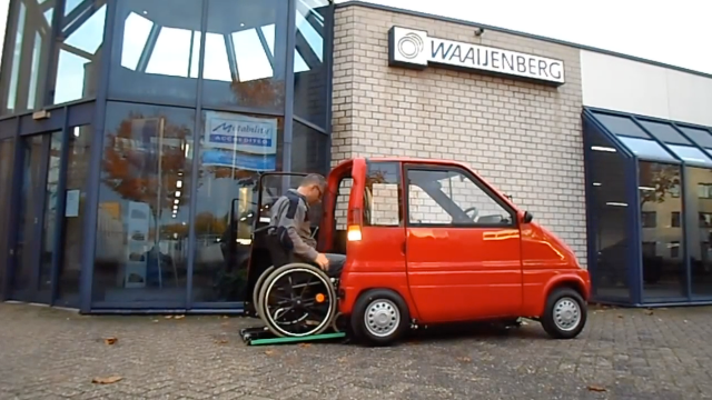 Foto des Mikroautos mit einfahrendem Mann im Rollstuhl