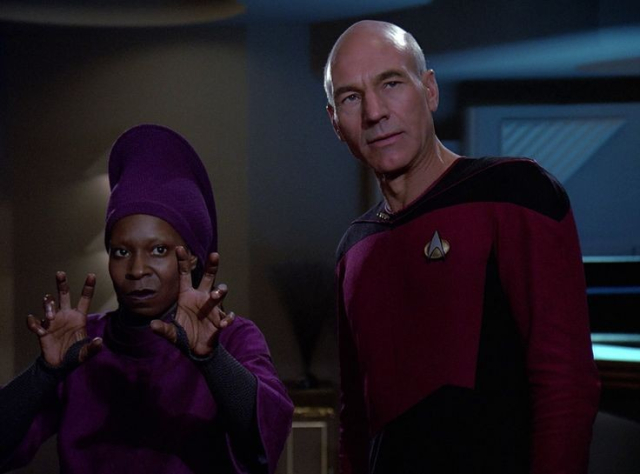 Guinan mit ausgespreizten Fingern in Abwehrhaltung, daneben Picard mit genervt-kritischem Blick; Reaktion auf Q aus Star Trek TNG (S02E16)