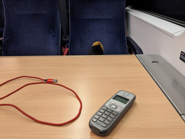 Foto aus dem ICE 4er mit Tisch, DECT Telefon, USB Kabel und Füße (ohne Schuhe) auf dem Sitz der gegenüber 