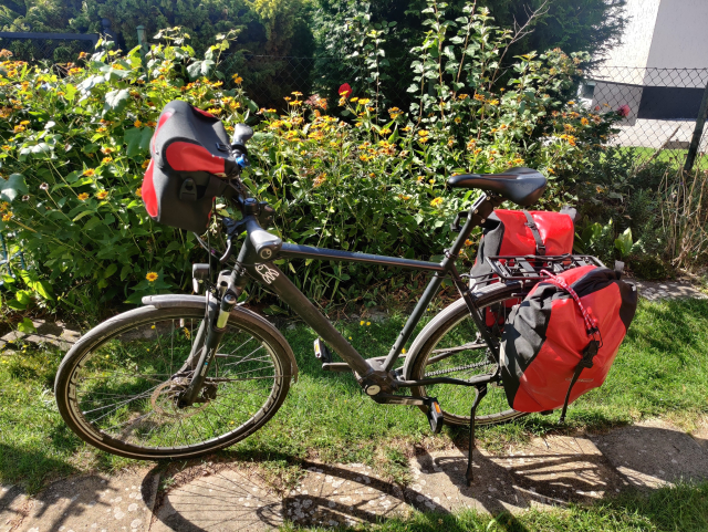 Schwarzes Fahrrad mit Fahrradtaschen vor einer Hecke im Sonnenschein.

Auf dem Rahmen ein Raketen Aufkleber.