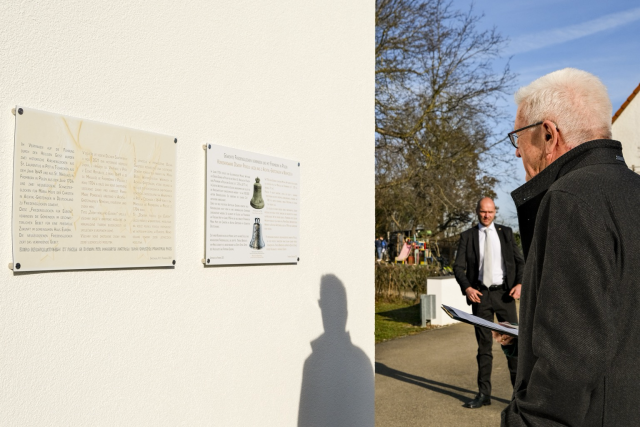 Baden-Württembergs Ministerpräsident Winfried Kretschmann liest die Gedenktafel zu den Friedensglocken am Kirchplatz Pfarrkirche Maria Hilf der katholische Kirchengemeinde Grötzingen.