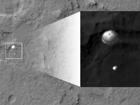 Curiosity as it is descending towards the surface of Mars, suspended from parachute in the Martian atmosphere, photographed from orbit by Mars Reconnaisance Orbiter in 2012 against the background of the cratered surface of Mars. Enlargement of detail in inset.