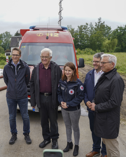 Ministerpräsident Kretschmann und Innenminister Strobl stehen mit Rettungskräften des Deutschen Roten Kreuz vor einem Feuerwehrauto in Erbach. 