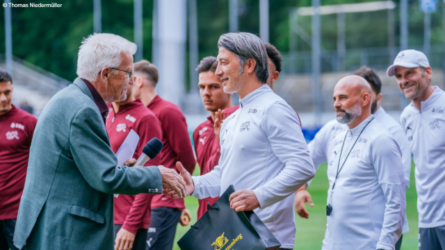 Ministerpräsident Kretschmann schüttelt dem Schweizer Nationaltrainer Murat Yakin die Hand und übergibt ihm ein Geschenk. Im Hintergrund sieht man Teile der Schweizer Fußball-Nationalmannschaft. Foto: Thomas Niedermüller