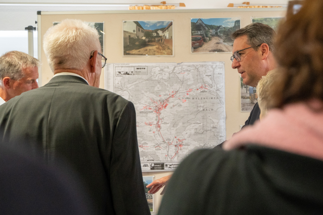 Ministerpräsident Kretschmann spricht mit dem Landrat des Rems-Murr-Kreises Dr. Richard Sigel. Vor ihm ist eine Karte mit Fotos der Hochwasser-Schäden aufgebaut.