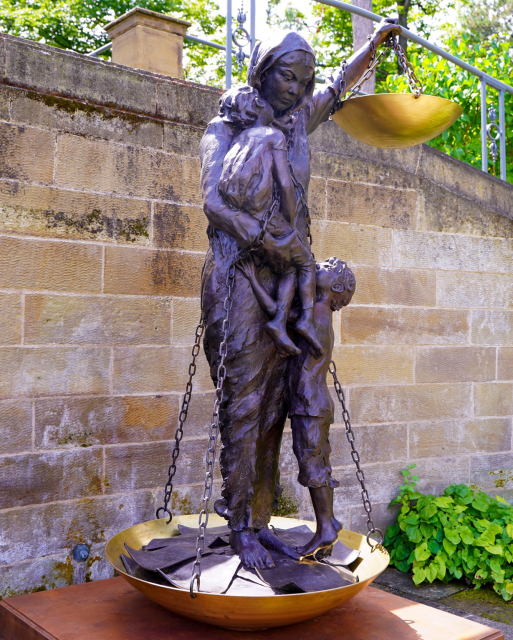 Lebensgroße Bronze-Statue einer Ezidin mit ihren Kindern und einer Waage der Gerechtigkeit im Park der Villa Reitzenstein.