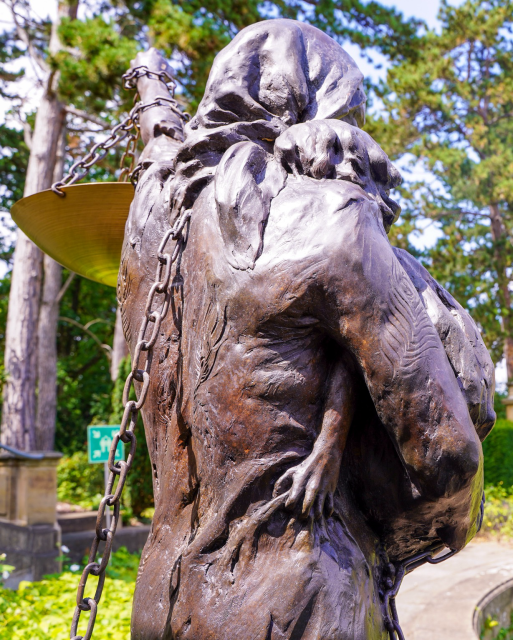 Rückansicht einer Bronze-Statue im Park der Villa Reitzenstein. Sie zeigt eine Ezidin mit ihren Kindern und einer Waage der Gerechtigkeit.