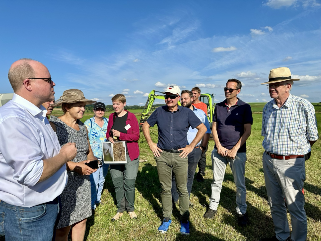 Ministerpräsident Winfried Kretschmann spricht auf einem Feld im Federseemoor mit anwesenden Experten und Praktikern.