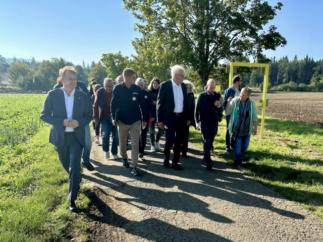 Ministerpräsident Kretschmann umringt von Vertreterinnen und Vertretern der Bürgerinitiative. Sie laufen auf einem Feldweg. Im Hintergrund sieht man Feldwege und Äcker.