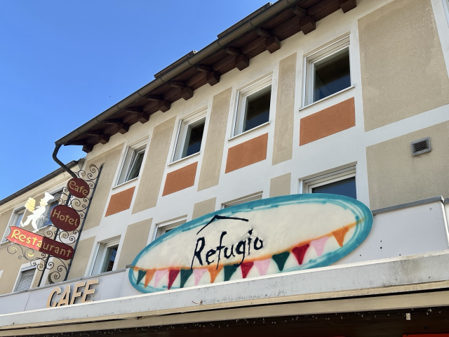 Fassade des Restaurant-Cafés Refugio. Das Schild mit der Aufschrift ist blau umrahmt und hat bunte Fähnchen unten.