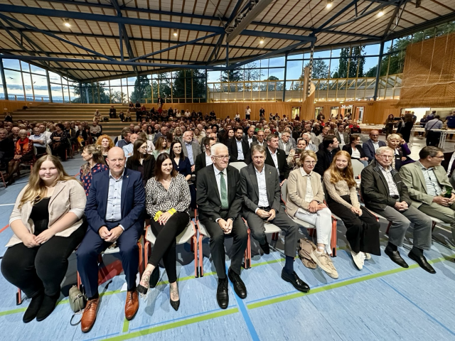 Ministerpräsident Kretschmann sitzt mit den Gästen des Bürgerempfangs in der Turnhalle von Geislingen.