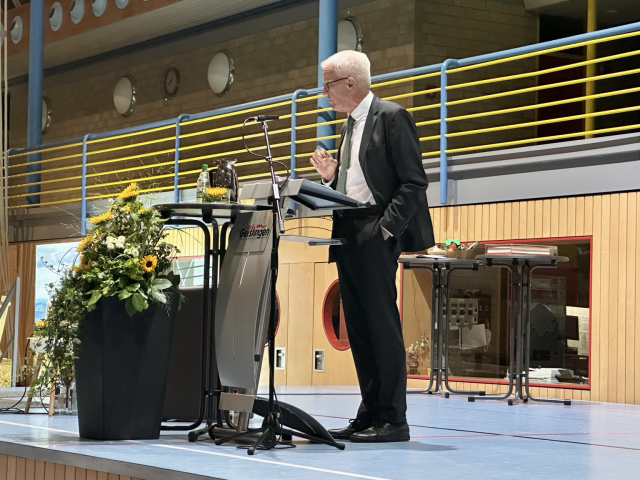 Kretschmann steht auf der Bühne der Turnhalle am Pult und hält eine Rede.