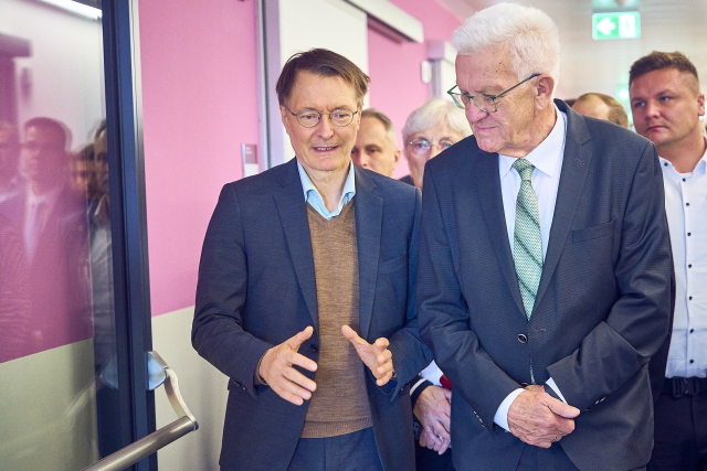 Bundesgesundheitsminister Karl Lauterbach und Ministerpräsident Winfried Kretschmann laufen nebeneinander her. Lauterbach spricht und gestikuliert mit den Händen. MP Kretschmann hat die Hände verschränkt und hört ihm zu.