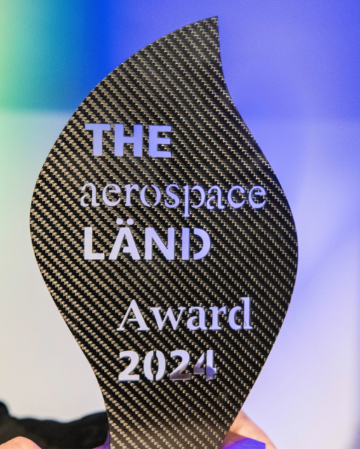 Foto vom The Aerospace Länd Award 2024. Er hat die Form einer grauen Flamme, die Schrift darauf ist durchsichtig.