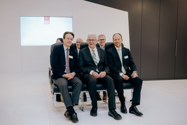 Ministerpräsident Kretschmann (Mitte) sitzt mit zwei Männern auf einer 3er-Reihe Flugsitze. Foto: Staatsministerium BW | Ilkay Karakurt 