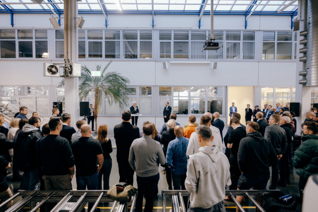 Sicht aus dem Publikum auf die Bühne, wo Ministerpräsident Winfried Kretschmann mit zwei weiteren Männern steht und eine Rede hält. Foto: Staatsministerium BW | Ilkay Karakurt