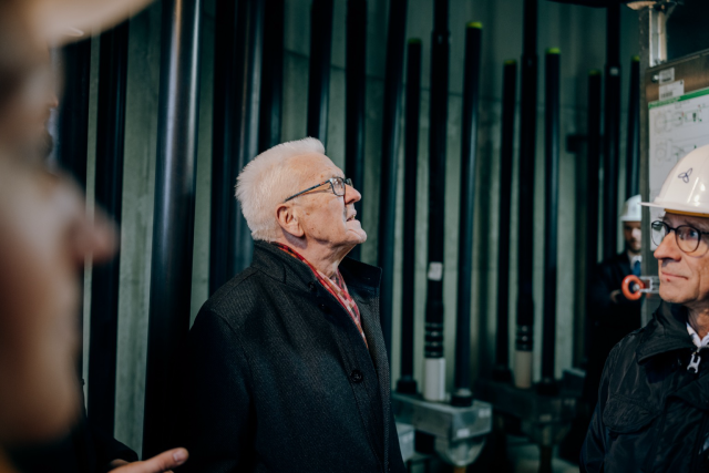 Ministerpräsident Winfried Kretschmann steht im Inneren eines Windrads und schaut nach oben. Auf dem Bild sind weitere Menschen im Vorder- und Hintergrund zu sehen, die zum Schutz weiße Helme tragen. © Staatsministerium BW | Ilkay Karakurt