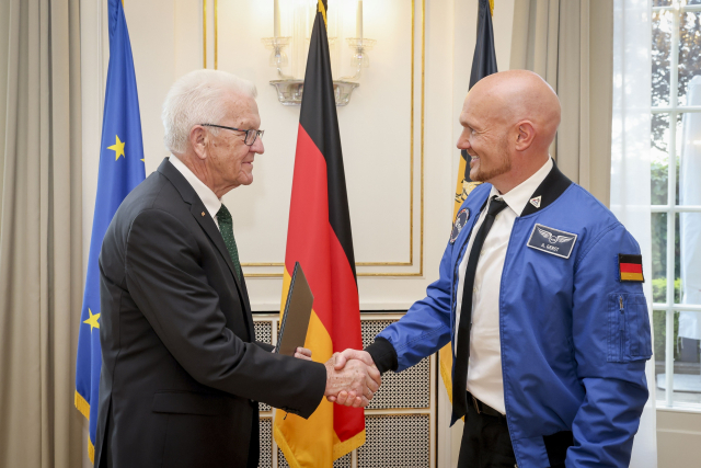 Ministerpräsident Kretschmann (links) und Alexander Gerst (links) schütteln sich in einem festlichen Raum die Hand, im Hintergrund EU-, Deutschland- und Baden-Württemberg-Flagge. © Staatsministerium Baden-Württemberg / Uli Regenscheit
