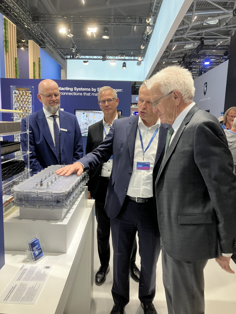 Ministerpräsident Kretschmann steht mit drei weiteren Männern vor einem Ausstellungsstück. Alle vier tragen einen Anzug.