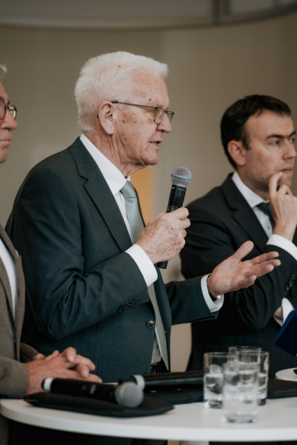 Innenminister Strobl (links), Ministerpräsident Kretschmann (mitte) mit Mikro und rechts PStS, Dr Schmid, MdB