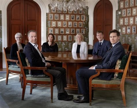 6 Leute, das Nobelpreis-kommitee, sitzen rund um Tisch in herrschaftlichen besprechungszimmer. 